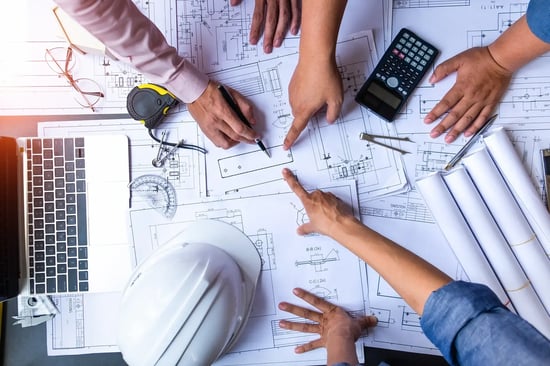 Project team reviewing blueprints, a laptop, and drafting tools at a desk